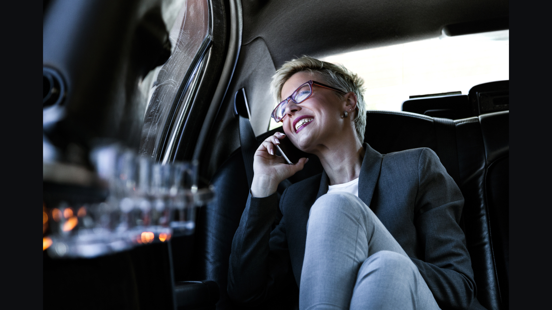 Client laughing on the phone in the back seat of a chauffeured car, lit by the city outside