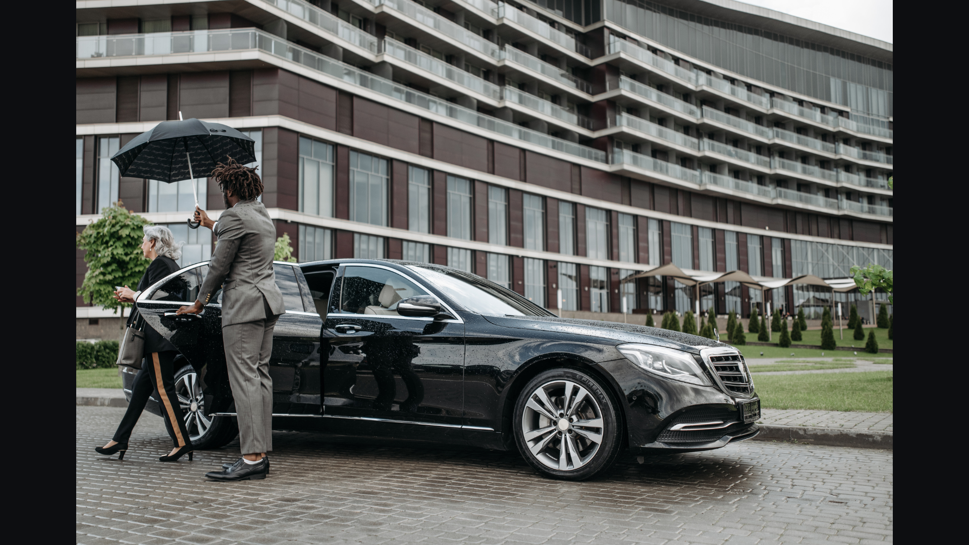 Luna chauffeur holding an umbrella while opening the door of a black sedan for a senior guest at the entrance of a Miami hotel